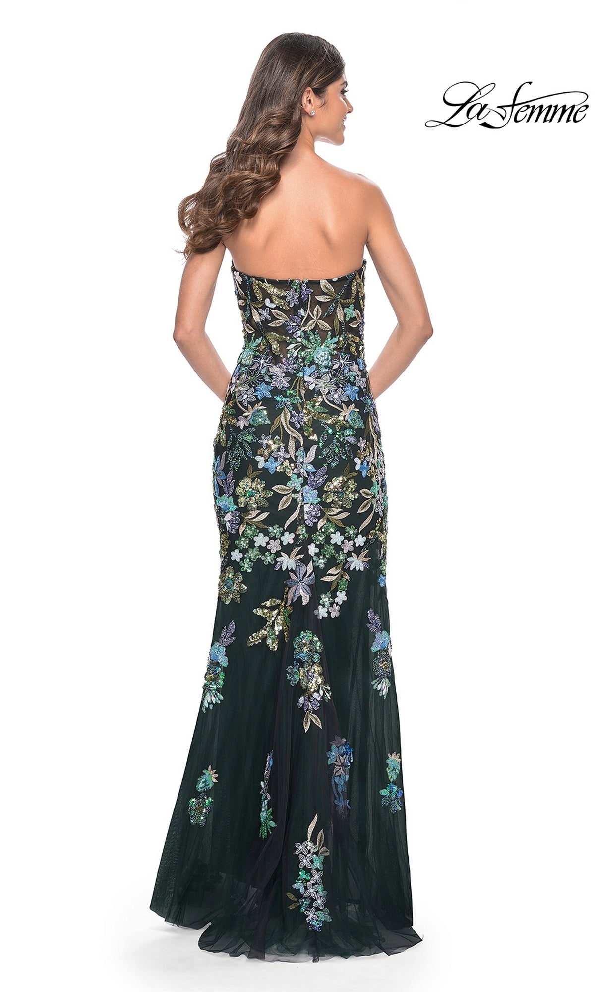 A woman with long wavy hair models the La Femme Strapless Sequin-Print Prom Dress 32251, a black floor-length strapless gown with colorful floral details, as seen from the back. The La Femme logo appears in the upper right corner.